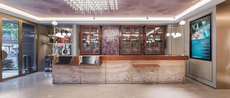 A modern hotel lobby with a marble reception desk, a digital screen, and a unique ceiling light fixture.