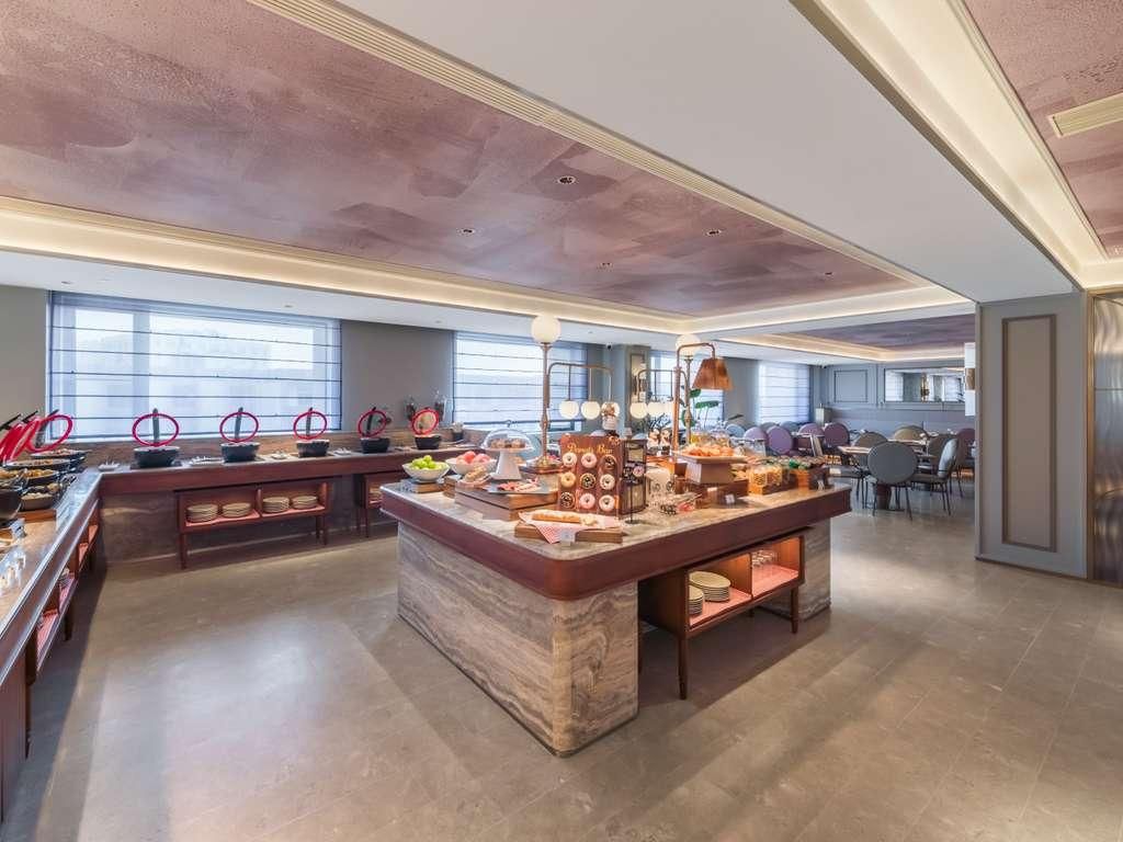 Buffet-alue, jossa on marmoritasoinen keskeinen pöytä, useita ruokatarjoilupisteitä ja erilaisia istumapaikkoja.