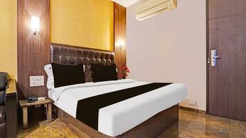 A hotel room with a bed, a nightstand, an air conditioning unit, and a door.