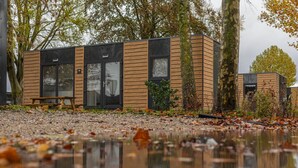 A modern building with large windows, a wooden exterior, and a bench outside. - Cube 95 | 4 persoons chalet in Zennewijnen (Zennewijnen)