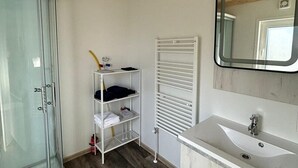 A bathroom with a glass shower enclosure, a white sink, a mirror, and a towel rack. - Cube 95 | 4 persoons chalet in Zennewijnen (Zennewijnen)