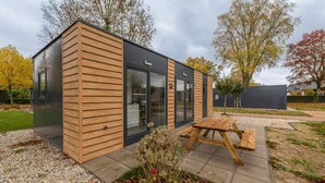 A modern building with a wooden exterior, large glass windows, and a patio with a wooden table. - Cube 95 | 4 persoons chalet in Zennewijnen (Zennewijnen)