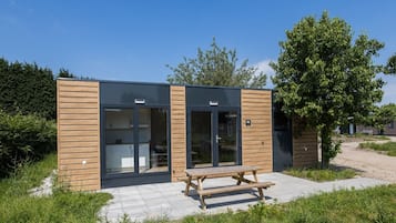 Een modern gebouw met een houten gevel, grote glazen deuren en een picknicktafel ervoor.