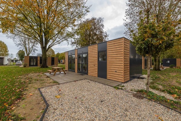 A modern outdoor building with a picnic table, surrounded by gravel and trees.