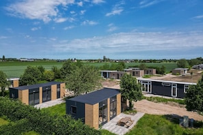 A modern residential area with compact housing units, a dirt path, and a large green field in the background.