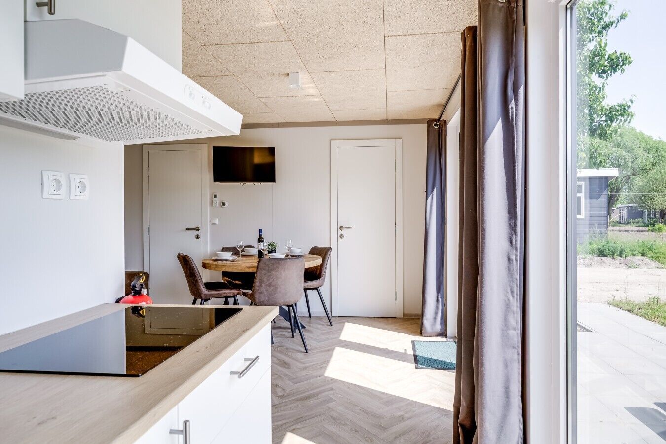 Une cuisine moderne avec un coin repas, un téléviseur à écran plat fixé au-dessus de la porte et une vue sur l’extérieur par une fenêtre.