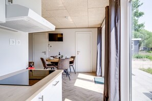 A modern kitchen with a dining area, a flat-screen TV mounted above the door, and a view of the outside through a window.