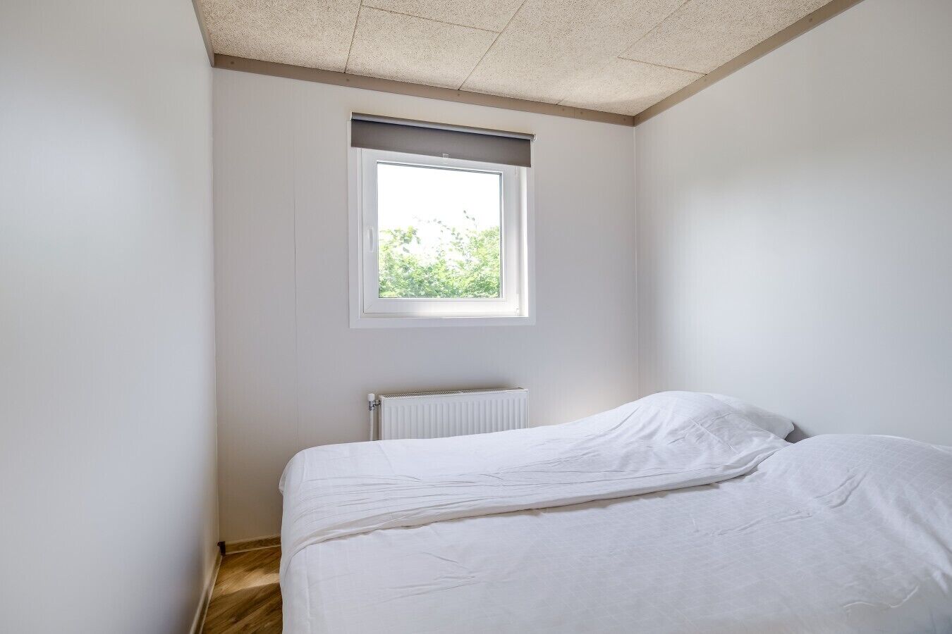 A small, single-bed room with a window, white walls, and a radiator.