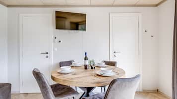 Een eetruimte met een ronde houten tafel, vier gestoffeerde grijze stoelen, een fles wijn en witte borden.