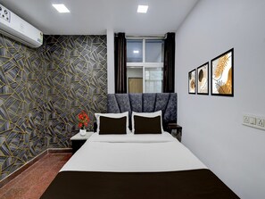 Ein modernes Schlafzimmer mit einer Wand mit geometrischem Muster, einem Bett mit dunkler Bettwäsche, einem Nachttisch mit Blumen in einer Vase und gerahmten Kunstwerken an der Wand.
