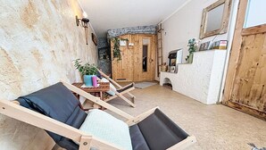 Une pièce comprenant deux fauteuils en bois, une petite table avec une plante, une porte en bois et un mur blanc à texture.
