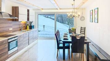 Cozinha moderna com área de refeições, piso de madeira e vista para uma paisagem nevada.