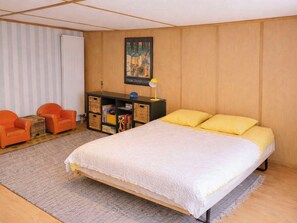 A bedroom with a bed, two chairs, a desk with storage, and a painting on the wall.