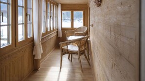 Un intérieur en bois avec un long couloir, de grandes fenêtres, des chaises en osier et une table.