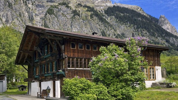 Un chalet traditionnel en bois, doté de fondations en pierre, de grandes fenêtres et offrant une vue sur un paysage montagneux.