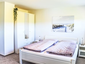 A bedroom with a bed, a wardrobe, a bedside table, a lamp, and a wall-mounted picture.