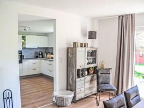 A modern kitchen with white cabinets, a dining area with a dark leather chair, and a wooden floor.