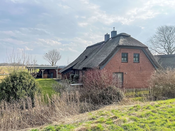 A traditional brick house with a steeply pitched roof, a small attached structure, and a fenced yard.