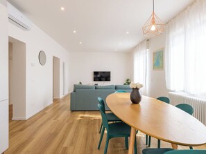Ein modernes Wohnzimmer mit einer Couch, einem Fernseher, einem Esstisch mit Stühlen und einer Vase mit Blumen.