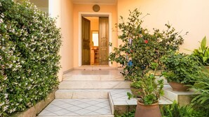 Un escalier menant à une porte, le tout entouré d’une végétation luxuriante et de plantes en pot.