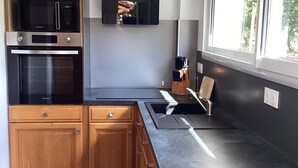 A modern kitchen with wooden cabinets, a built-in microwave, oven, and a large window. - Mas des Chênes.  Private spa. Nature and tranquility   (La Baume-de-Transit)
