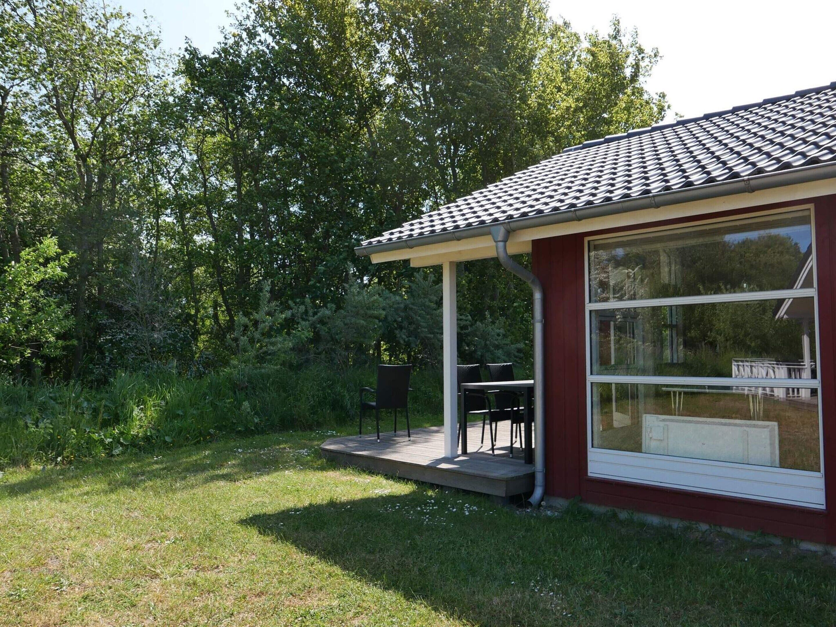 A small house with a covered patio, a large window, and a garden.