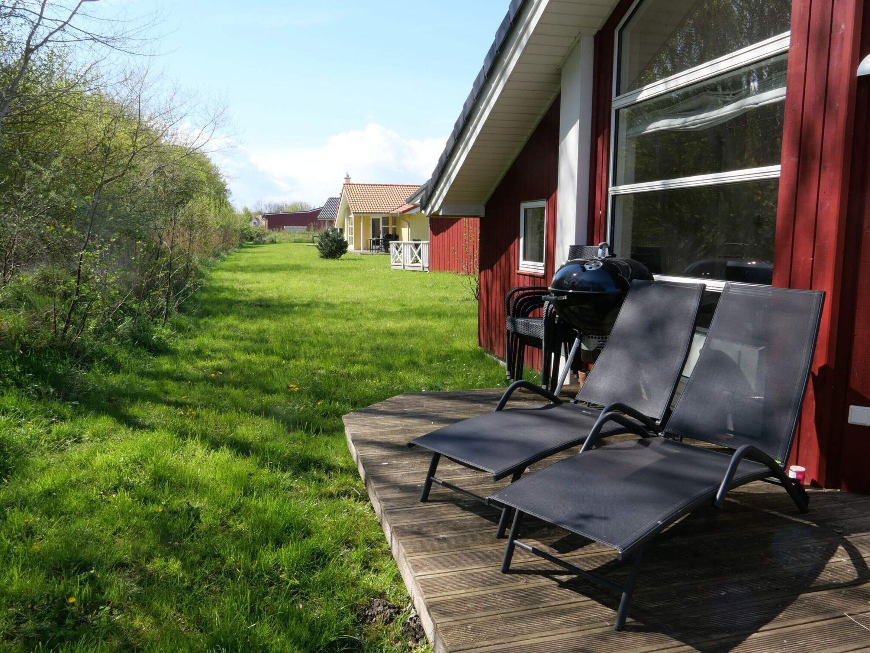 A wooden deck with two sun loungers, a barbecue grill, and a red building with a window.