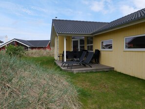A yellow building with a tiled roof, a covered patio with outdoor furniture, and a grassy yard. - 4 Star Holiday Home in Grossenbrode (Grossenbrode)