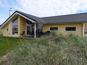 A yellow house with a large porch, a chimney, and a grassy yard. - Base With Private Sauna, Sun Deck (Grossenbrode)