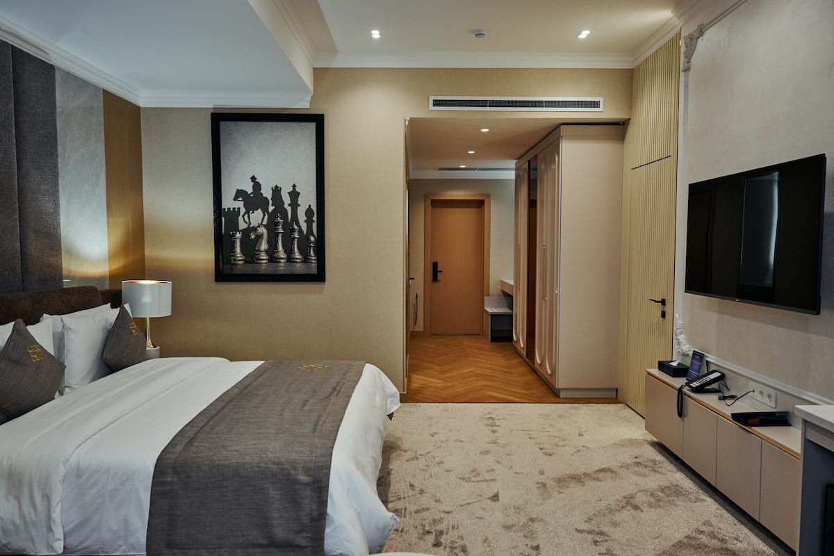 A hotel room with a bed, a television, a framed chessboard, and a wardrobe.