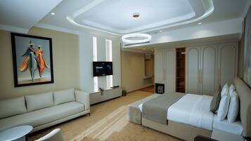 A modern hotel room with a sofa, a bed, a TV, and a painting on the wall.