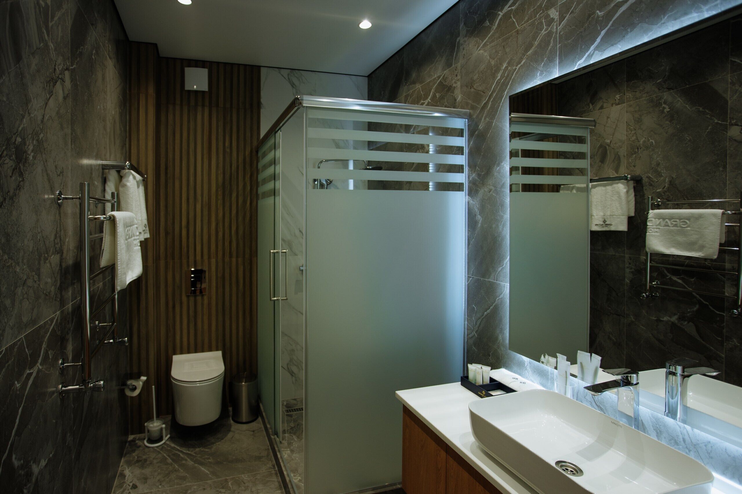 Un baño moderno con ducha de vidrio, lavamanos blanco y un espejo grande, además de paredes de mármol.