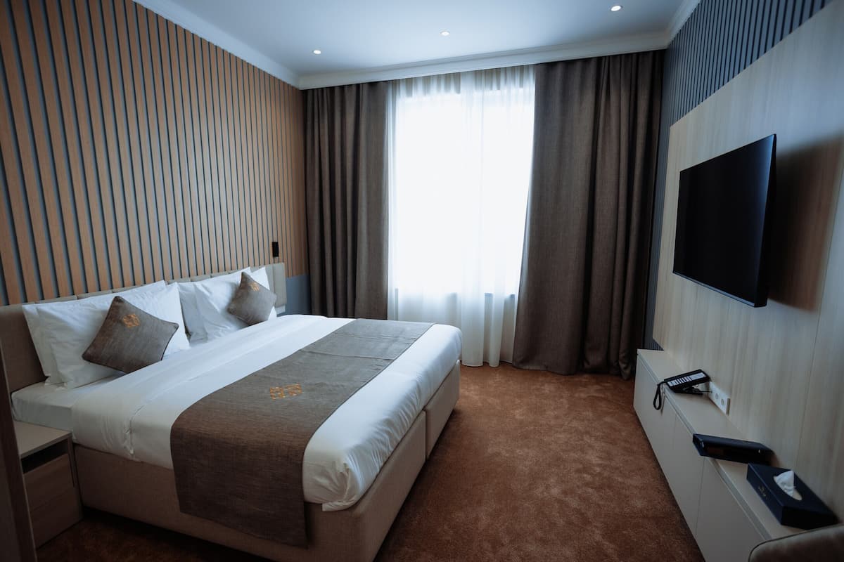 A hotel room with a large bed, a TV mounted on the wall, and a window with curtains.