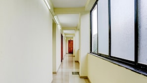 Un pasillo largo y estrecho con suelo de baldosas, ventanas grandes a un lado y puertas espaciadas.