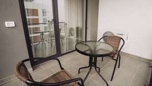 Un balcón con puerta de vidrio, dos sillas de mimbre, una mesa redonda y un aire acondicionado instalado en la pared.
