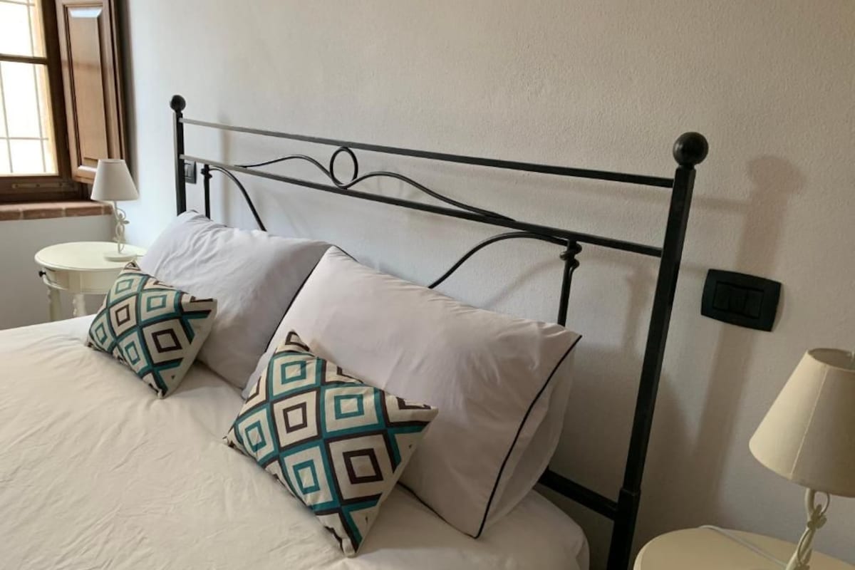 A bed with a metal frame, two patterned pillows, a white bedspread, and a bedside table with a lamp.