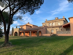 A large, multi-story building with a courtyard, featuring a mix of brick and stucco exteriors, arched doorways, and a prominent tree. - Villa Preselle Country Resort (Preselle)