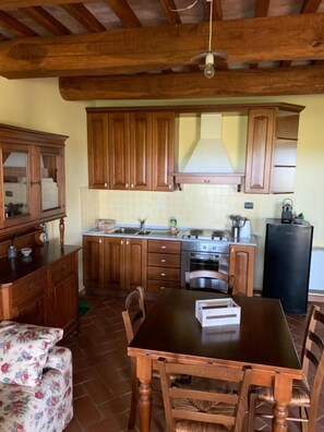 A kitchen with wooden cabinets, a stove, and a dining table with chairs. - Villa Preselle Country Resort (Scansano)