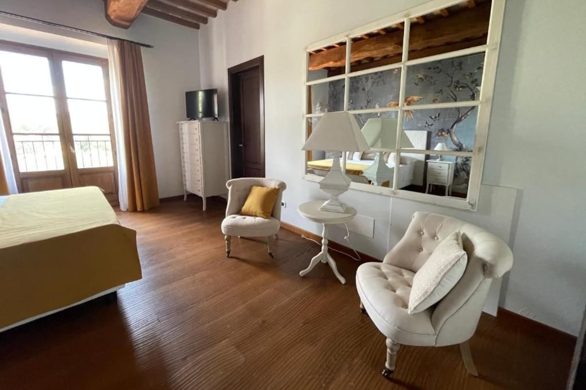 A room with a bed, two armchairs, a small table, a window with a view, and a cabinet.