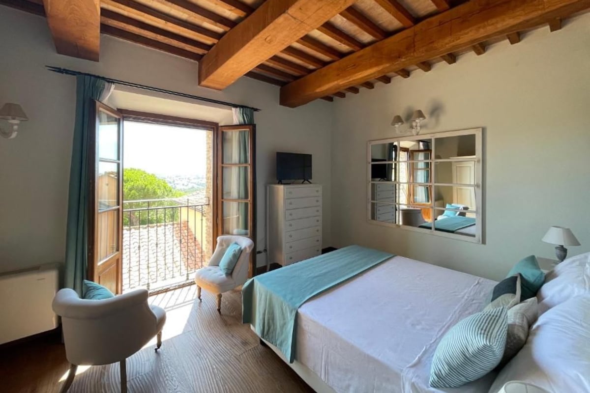 A bedroom with a large bed, a chair, a dresser, a TV, and a balcony with a view.