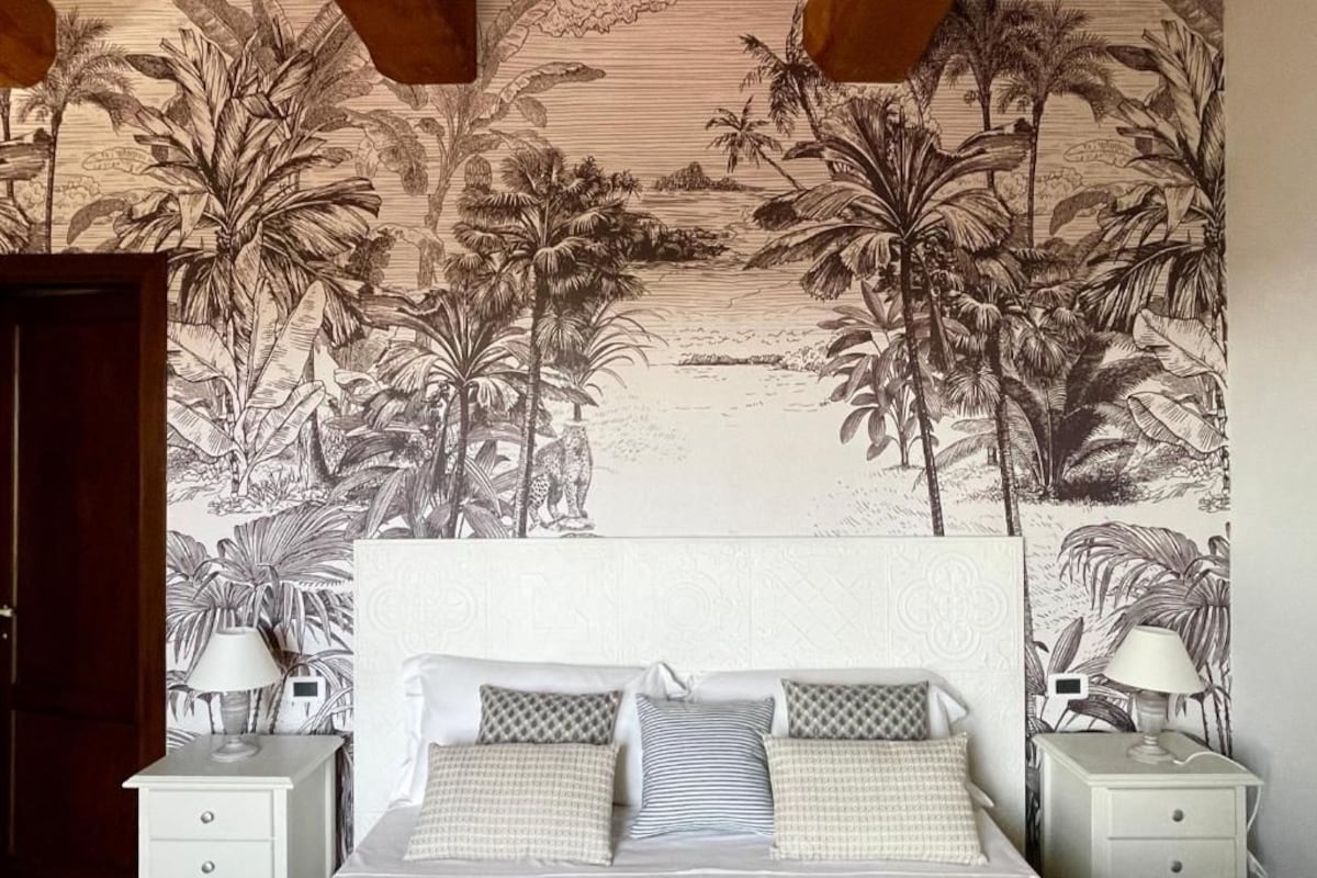 A bedroom with a bed, two bedside tables, and a tropical-themed wall mural.