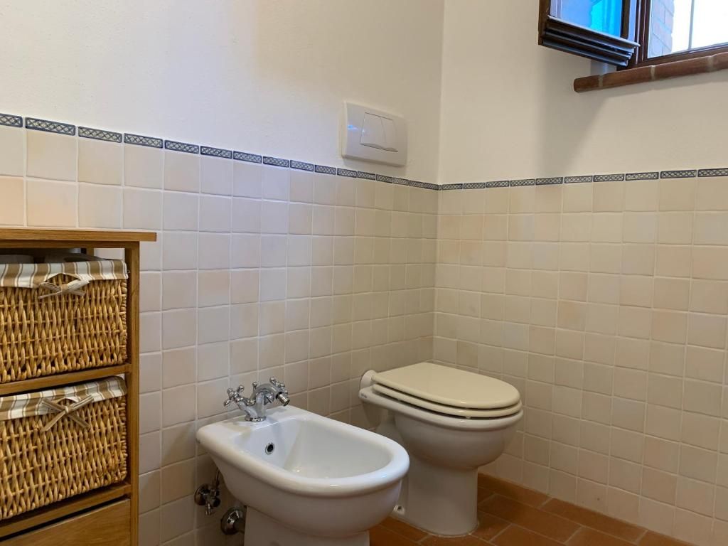 A bathroom with white tiled walls, a wooden vanity with wicker baskets, a bidet, and a toilet.