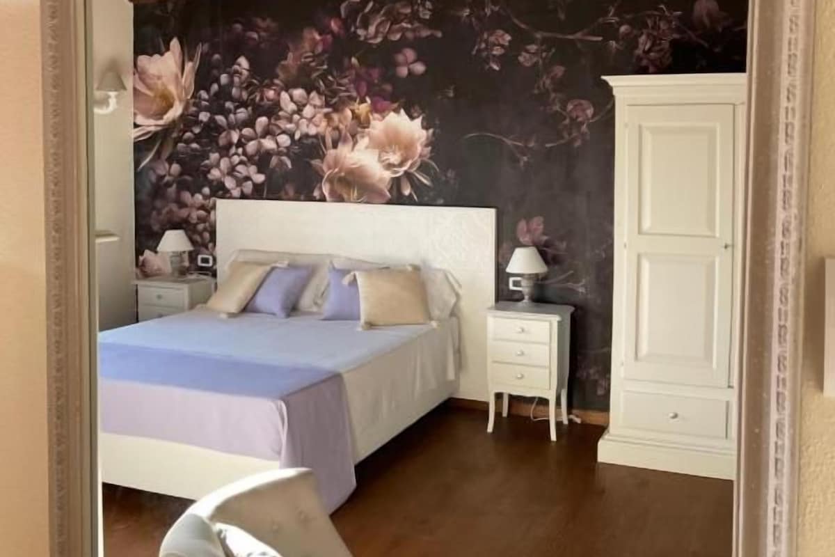 A bedroom with a bed, nightstands, a wardrobe, and a floral wallpaper.