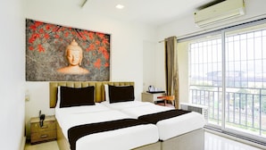 Ein Hotelzimmer mit einem großen Bett, einem Nachttisch, einem Buddha-Gemälde und Blick aus dem Fenster.