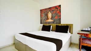 Ein Hotelzimmer mit einem großen Bett, einem Kopfteil mit einem Buddha-Gemälde, einem kleinen Tisch mit Tassen und einem Sessel.