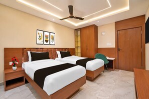 Une chambre d’hôtel avec deux lits, un ventilateur de plafond, des spots encastrés, un bureau et une porte.