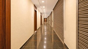 A long, narrow hallway with closed doors on both sides, a shiny tiled floor, and recessed ceiling lights.
