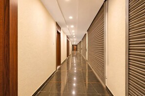 A long, narrow hallway with closed doors on both sides, a shiny tiled floor, and recessed ceiling lights.