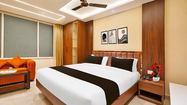 A hotel room with a large bed, a bedside table with a phone and a vase of flowers, a seating area with a sofa and a tray table, and artwork on the wall.