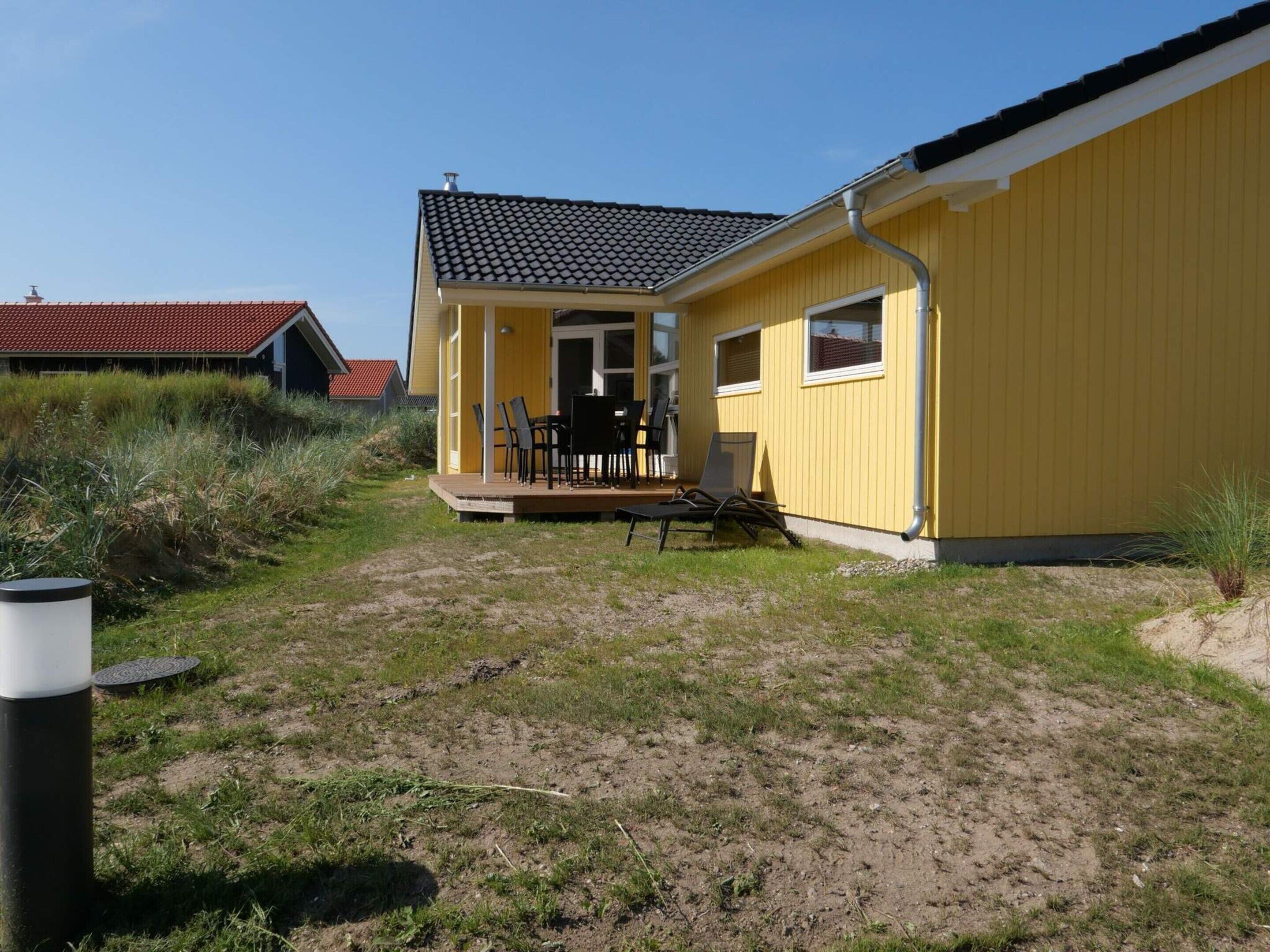 A yellow building with a tiled roof, a porch with chairs, and a small deck.